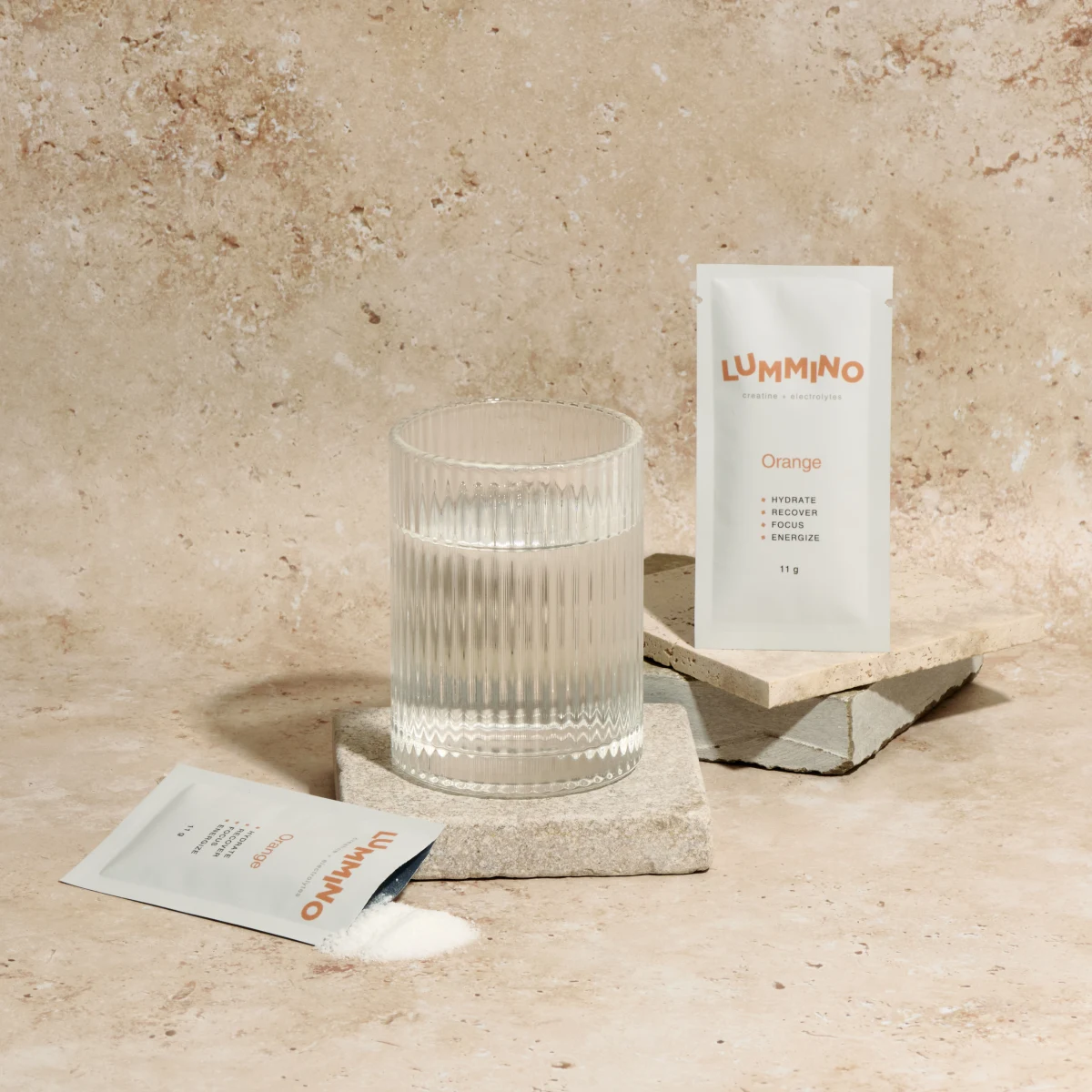 A sachet of Lummino beside a glass of clear orange drink that dissolves clear