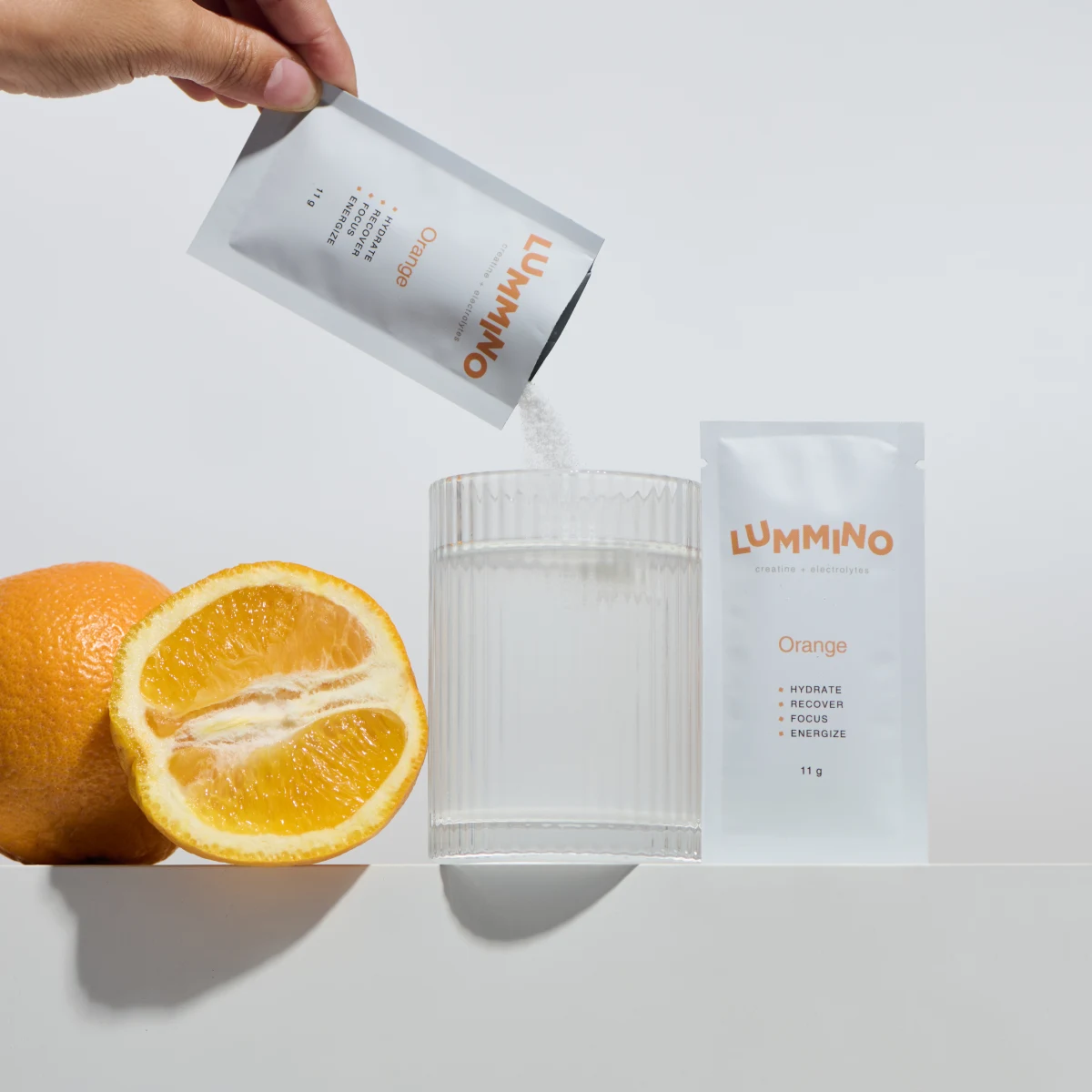 Lummino creatine and electrolytes in orange, shown with a clear orange drink